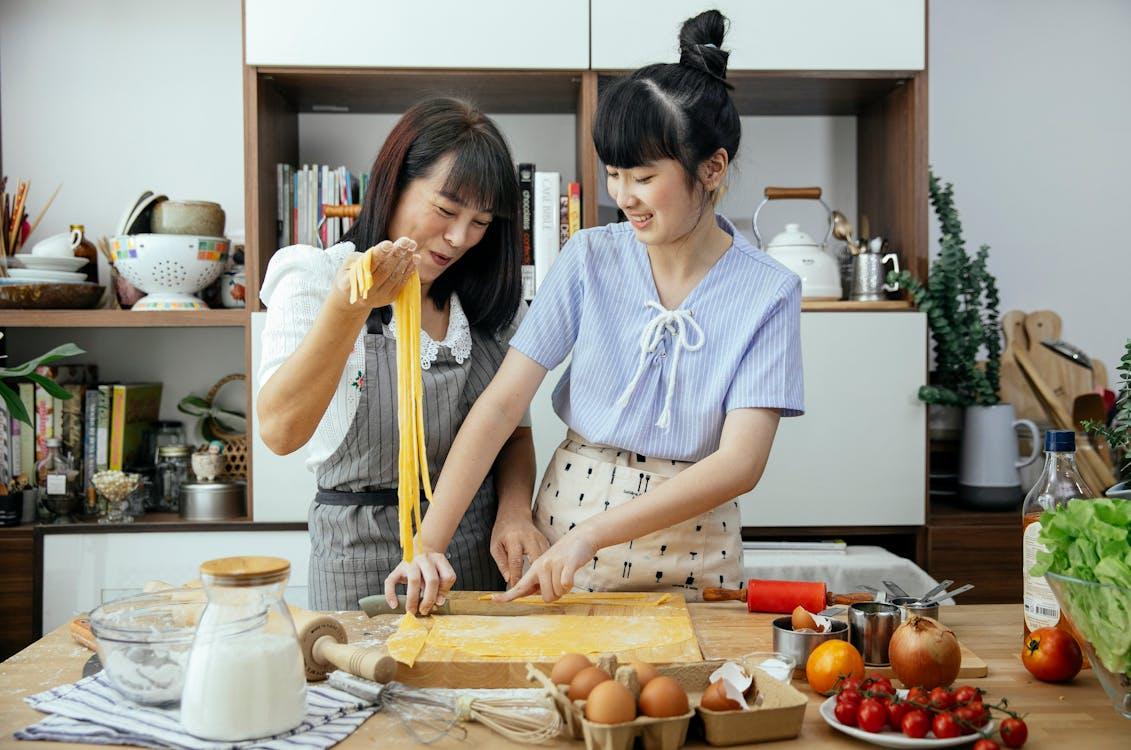 A female domestic helper showing her employer's daughter how to prepare food in the kitchen